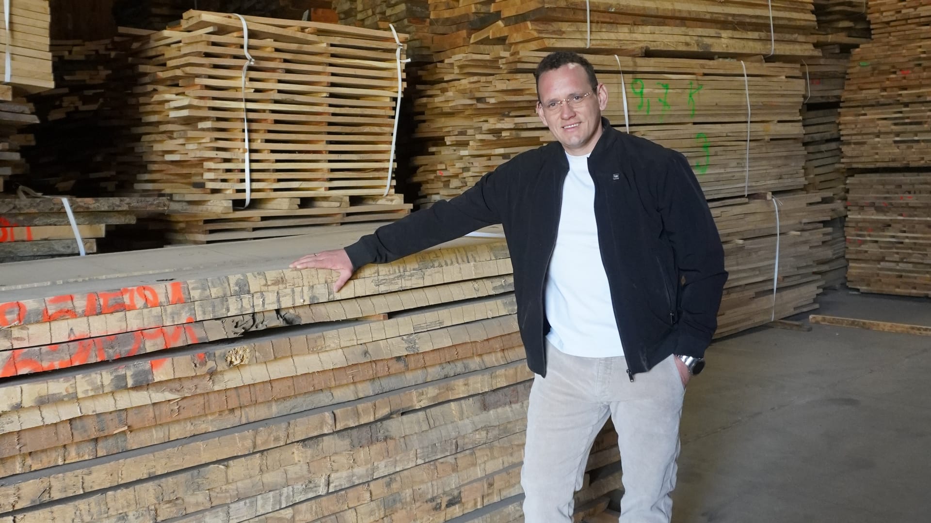 Mann am Schnittholzstapel in der Halle, Hand auf dem Paket